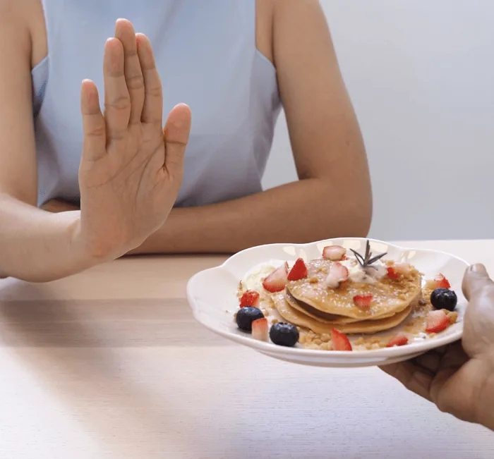A hand declining a plate of pancakes